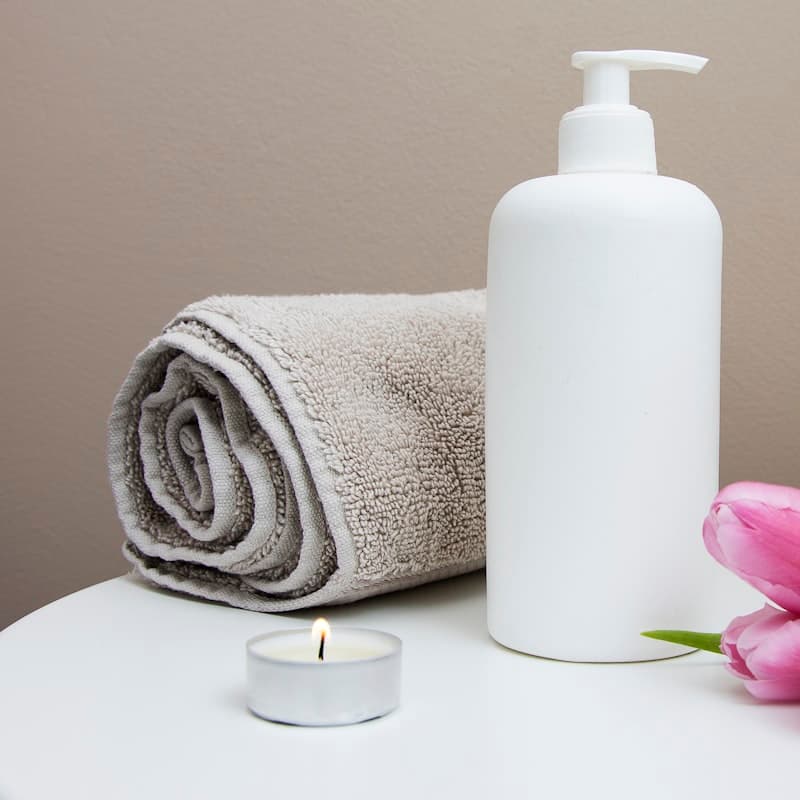 Fresh folded towel, massage lotion and a lit candle at the spa