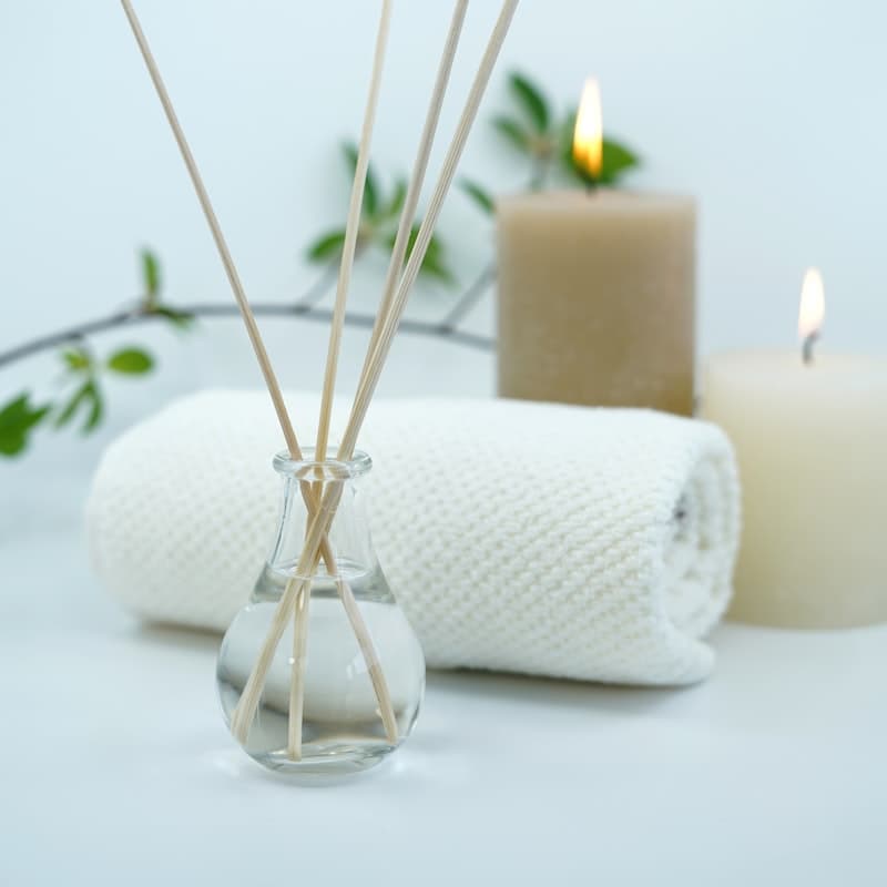 Reed diffuser, candles and a rolled towel in a calm spa corner